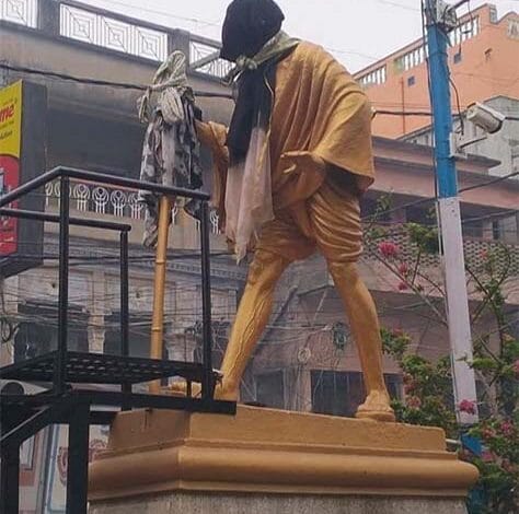 बंगाल में महात्मा गांधी की प्रतिमा के चेहरे पर काला कपड़ा डाला गया है। यह तस्वीर गांधी की प्रतिमा को लेकर उभरे विवाद और राजनीतिक असहमति का प्रतीकात्मक दृश्य दर्शाती है।