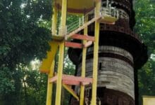 कोदोभाट में जल जीवन मिशन योजना का सूचना बोर्ड और क़ुतुब मीनार की प्रतिबिम्ब वाली प्रतीकात्मक तस्वीर